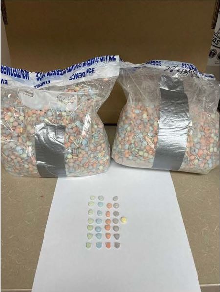 Photo of 2 large bags of multi-colored pills and a piece of paper with 5 lines of pills of each color and shape.